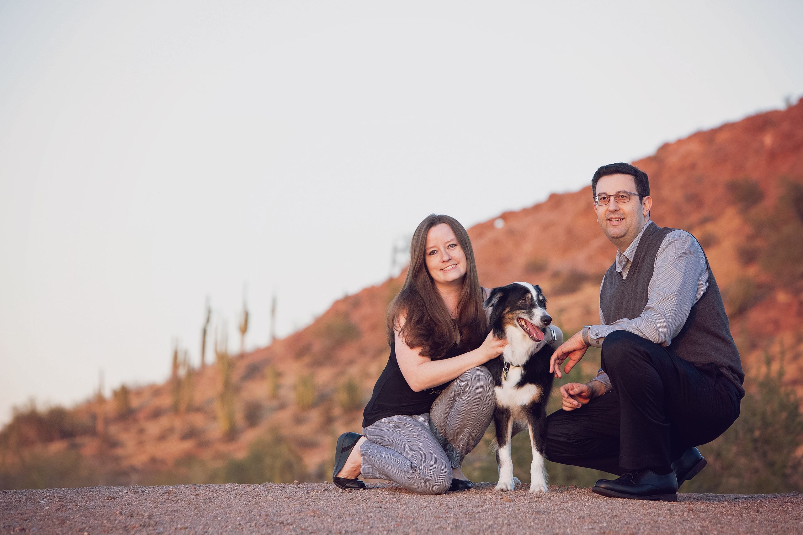 Dr. Berman and Dr. Kitchen crouched with their dog on a red Sonoran hillside at golden hour
